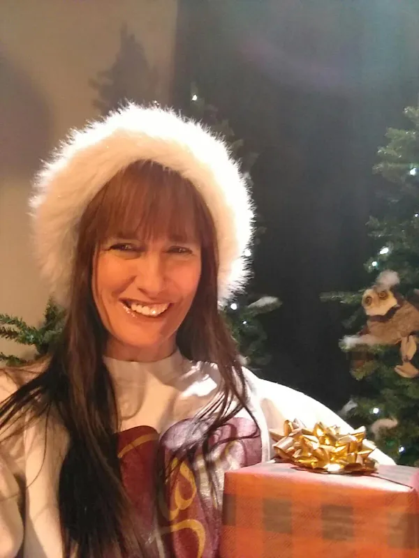 Woman in a Santa hat holding a wrapped gift by a Christmas tree